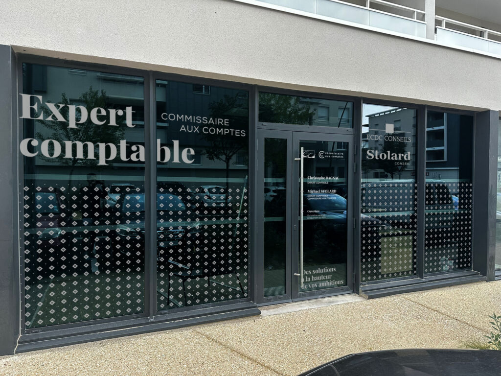 Cette image montre la devanture moderne d'un cabinet comptable situé à Les Angles. Sur les vitres, on peut lire les inscriptions "Expert comptable" et "Commissaire aux comptes", avec les noms de Christophe Magnac et Michael Stolard, indiquant qu'ils exercent au sein du cabinet. Le logo ECDC Conseils apparaît également sur la porte d'entrée. La façade vitrée, sobre et professionnelle, reflète l'engagement du cabinet à fournir des services comptables et financiers de qualité aux entreprises locales.